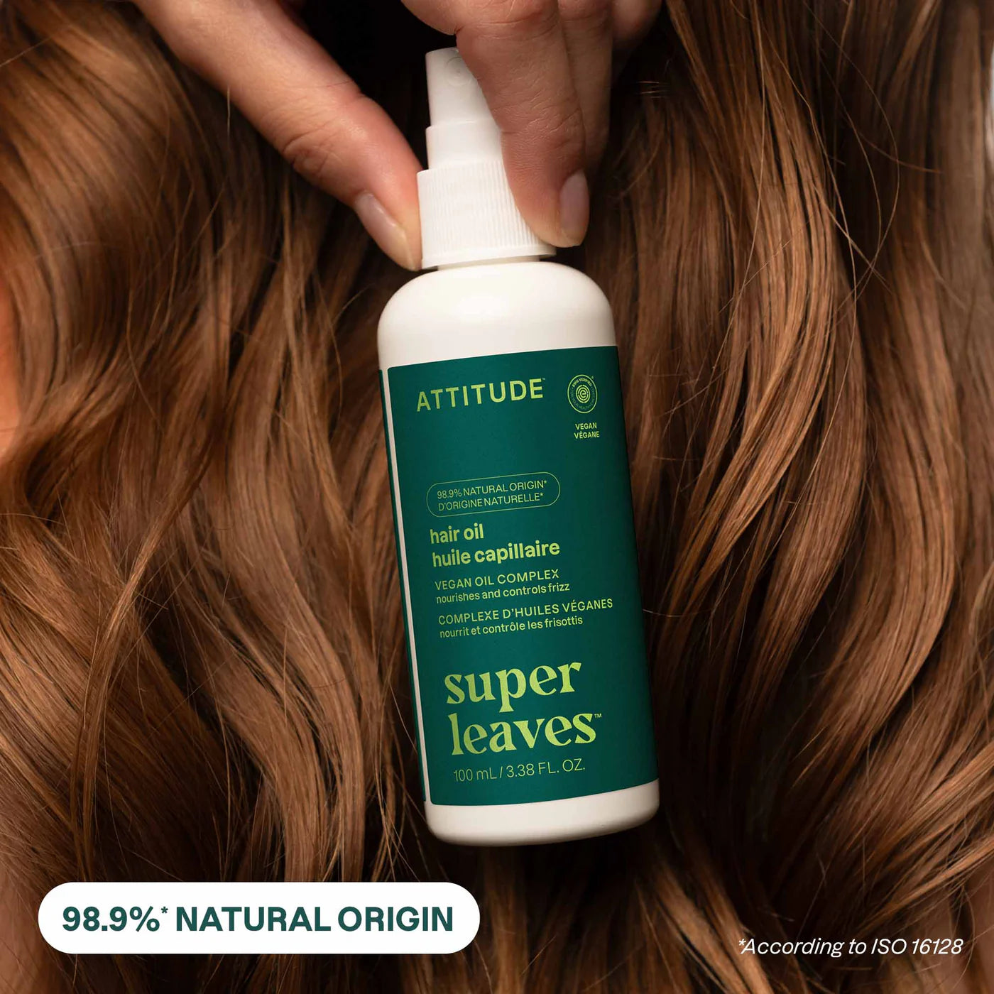 Bottle of Attitude super leaves hair oil held against wavy brown hair